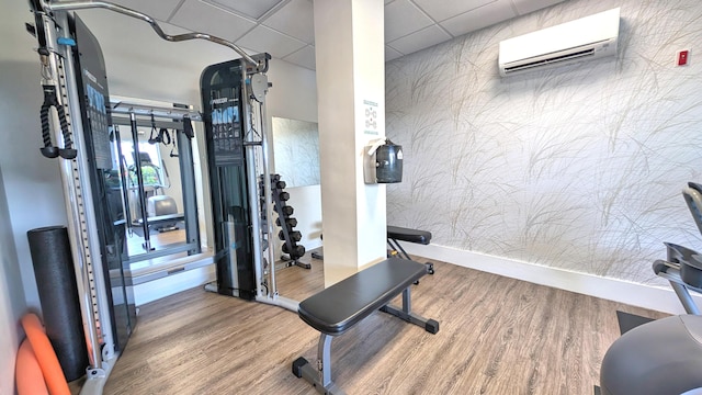 exercise room with a wall mounted air conditioner, hardwood / wood-style flooring, and a drop ceiling