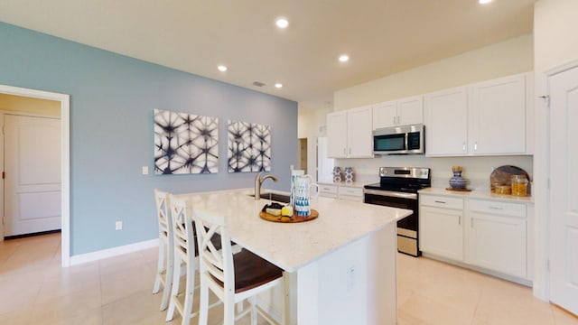 kitchen with a kitchen island with sink, white cabinets, sink, light tile patterned floors, and stainless steel appliances