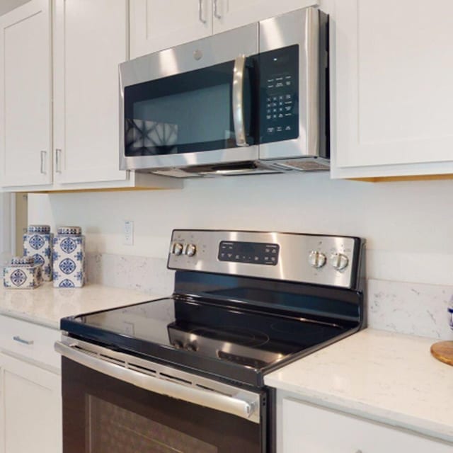 kitchen with white cabinets, light stone counters, and appliances with stainless steel finishes