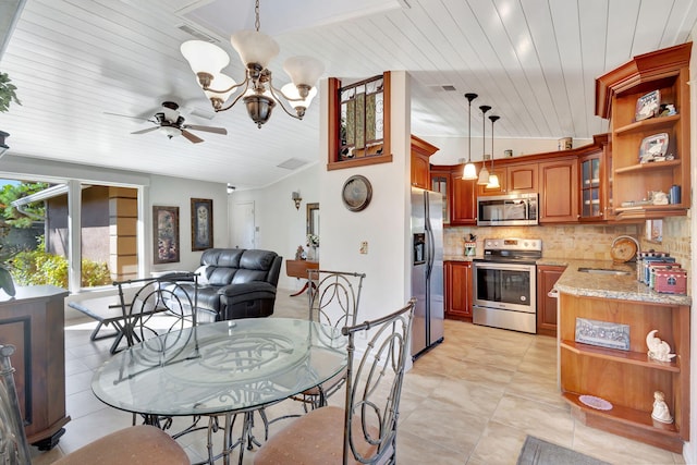 kitchen with light stone countertops, appliances with stainless steel finishes, ceiling fan with notable chandelier, vaulted ceiling, and pendant lighting