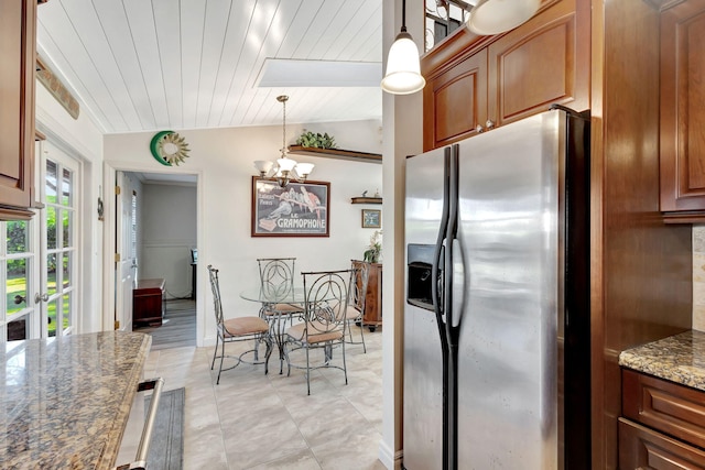 kitchen with wooden ceiling, dark stone counters, vaulted ceiling with skylight, stainless steel fridge, and decorative light fixtures