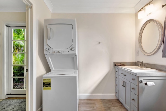 washroom with stacked washing maching and dryer, light hardwood / wood-style flooring, crown molding, and sink