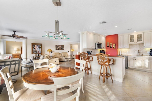 tiled dining room with ceiling fan, crown molding, and sink