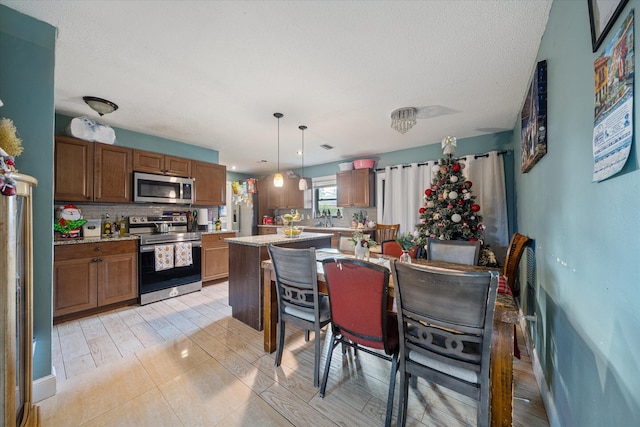 kitchen featuring a center island, hanging light fixtures, stainless steel appliances, a textured ceiling, and decorative backsplash