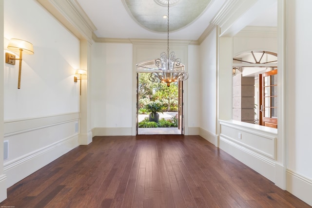 unfurnished dining area featuring a raised ceiling, dark wood-type flooring, a chandelier, and ornamental molding