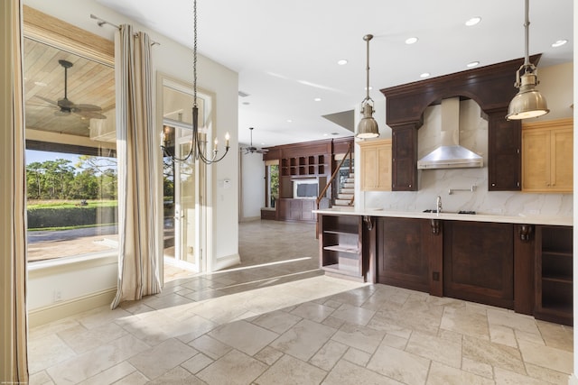 kitchen featuring decorative backsplash, ceiling fan with notable chandelier, a wealth of natural light, and wall chimney exhaust hood