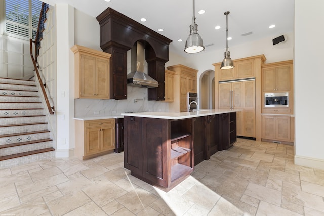 kitchen featuring wall chimney exhaust hood, hanging light fixtures, paneled fridge, tasteful backsplash, and a large island with sink