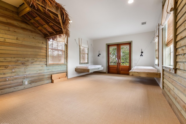 unfurnished bedroom featuring access to exterior, wood walls, french doors, and carpet