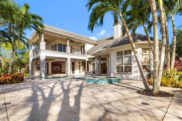 back of house featuring ceiling fan, a pool with hot tub, a balcony, and a patio area