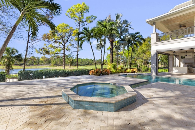 view of pool featuring ceiling fan, a patio area, a water view, and an in ground hot tub