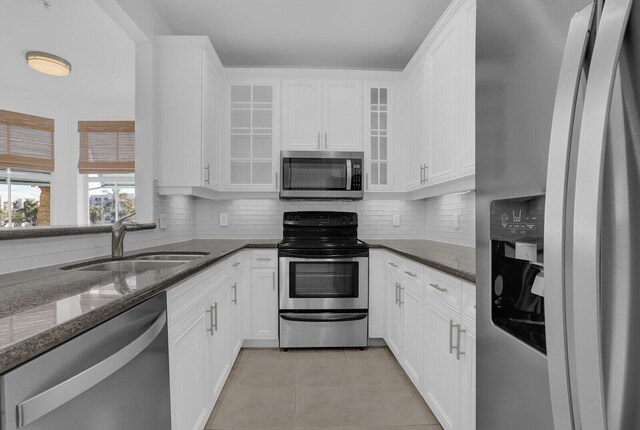 kitchen with backsplash, white cabinets, sink, dark stone countertops, and stainless steel appliances