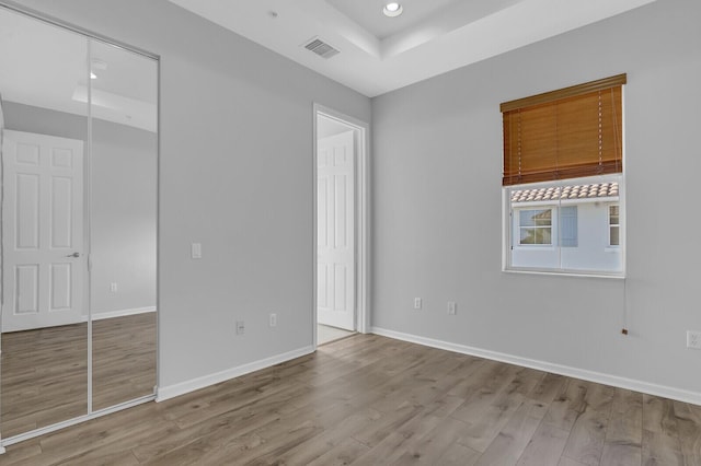 unfurnished bedroom with light hardwood / wood-style floors, a raised ceiling, and a closet