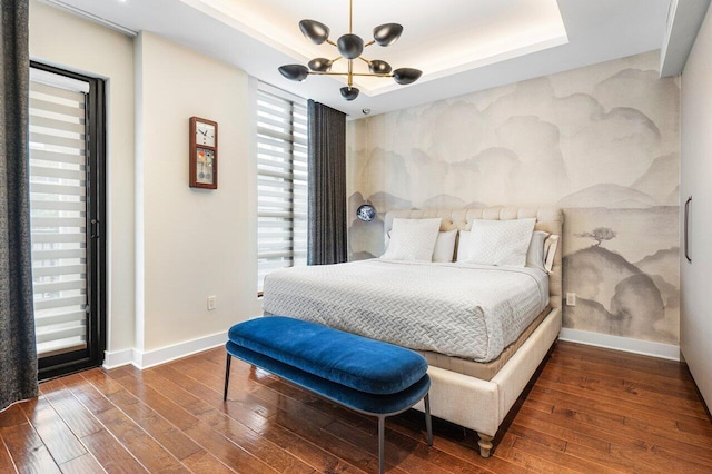 bedroom with a raised ceiling, dark hardwood / wood-style flooring, and a notable chandelier