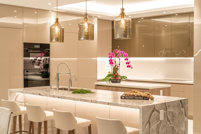 kitchen with a large island, white cabinetry, double oven, hanging light fixtures, and light stone counters