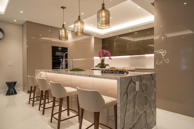 bar featuring light stone counters, black double oven, a tray ceiling, gray cabinets, and hanging light fixtures