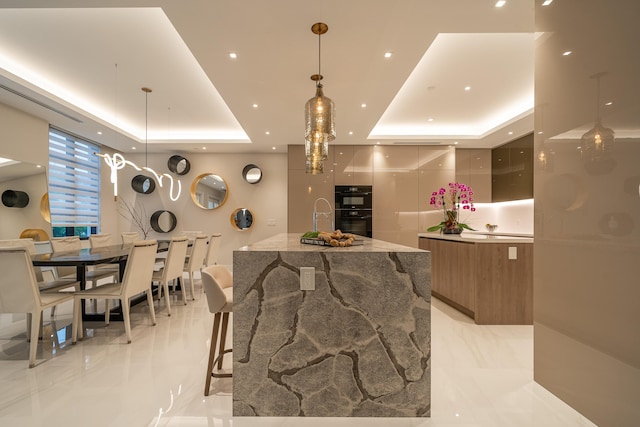 interior space featuring sink, a tray ceiling, double oven, pendant lighting, and a large island