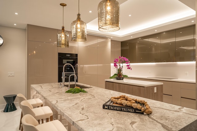 kitchen with sink, a kitchen bar, black double oven, a large island, and light stone countertops