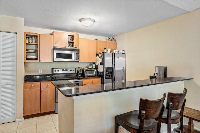 kitchen with kitchen peninsula, dark stone counters, a textured ceiling, stainless steel appliances, and light tile patterned floors