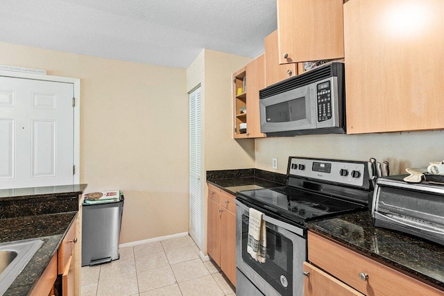 kitchen with light tile patterned flooring, dark stone counters, a textured ceiling, and appliances with stainless steel finishes