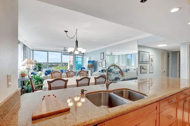 kitchen with sink, crown molding, decorative light fixtures, light stone countertops, and a notable chandelier