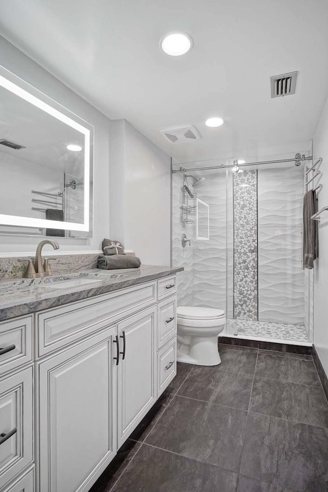 bathroom with tile patterned flooring, vanity, toilet, and tiled shower