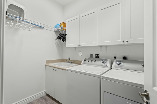 clothes washing area featuring hardwood / wood-style floors, washing machine and dryer, sink, and cabinets