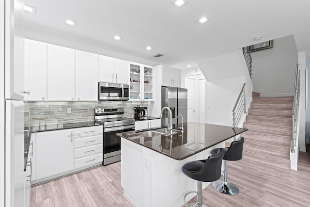 kitchen featuring backsplash, stainless steel appliances, sink, white cabinetry, and an island with sink