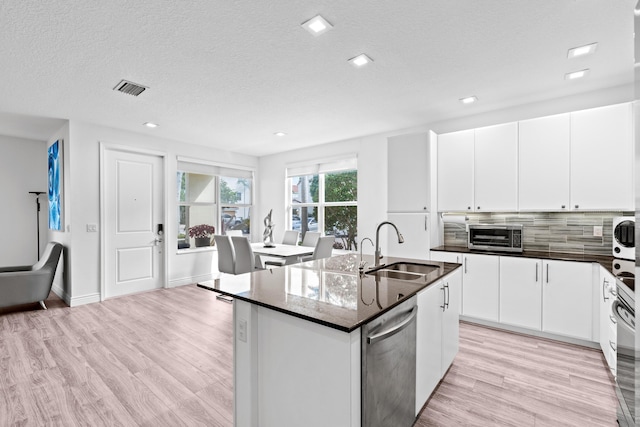 kitchen featuring dishwasher, sink, decorative backsplash, an island with sink, and white cabinetry