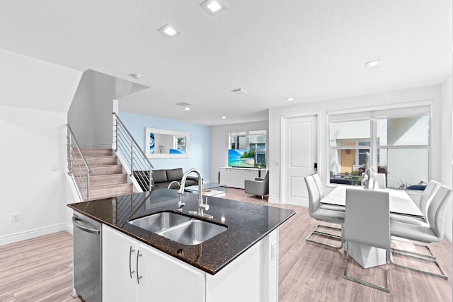 kitchen with white cabinetry, dishwasher, sink, light hardwood / wood-style flooring, and an island with sink