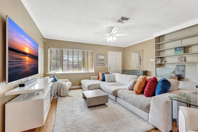 living room with a textured ceiling, light wood-type flooring, ceiling fan, and ornamental molding