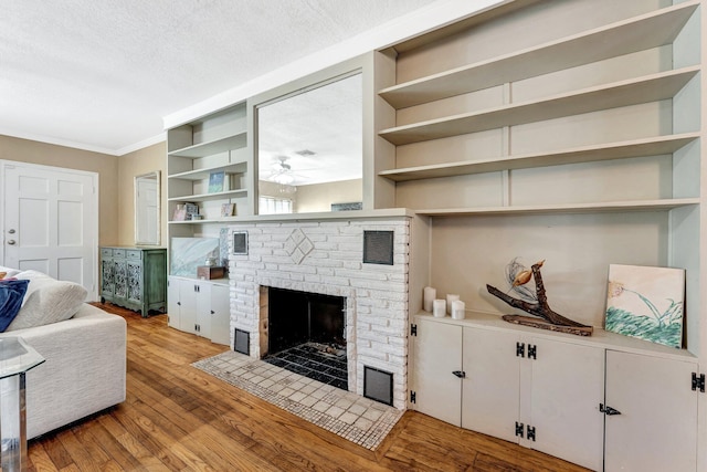 living room featuring light wood-type flooring, a brick fireplace, ornamental molding, a textured ceiling, and ceiling fan