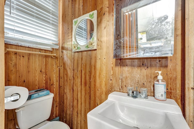 bathroom featuring toilet, wooden walls, and sink