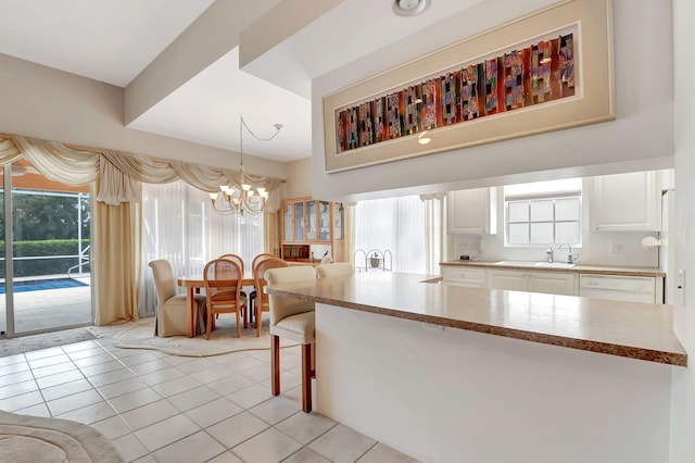 kitchen featuring sink, light tile patterned floors, pendant lighting, an inviting chandelier, and white cabinets