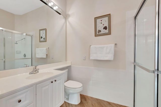 bathroom featuring vanity, wood-type flooring, tile walls, toilet, and a shower with shower door