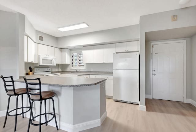 kitchen featuring kitchen peninsula, white appliances, white cabinetry, and a breakfast bar area