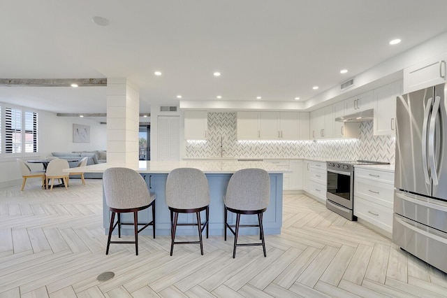 kitchen with white cabinetry, light parquet floors, a kitchen bar, tasteful backsplash, and appliances with stainless steel finishes