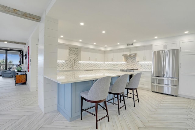 kitchen featuring a breakfast bar area, light stone countertops, stainless steel fridge, white cabinets, and sink