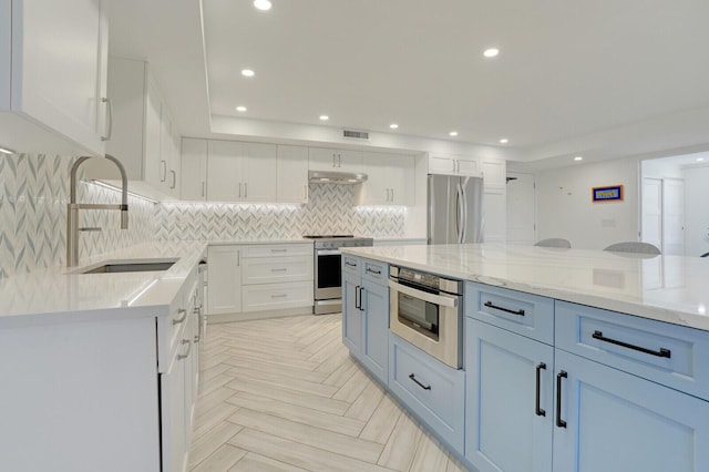 kitchen featuring stainless steel appliances, sink, white cabinets, light parquet flooring, and light stone countertops