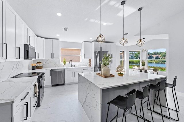 kitchen featuring white cabinets, hanging light fixtures, vaulted ceiling, appliances with stainless steel finishes, and a kitchen island