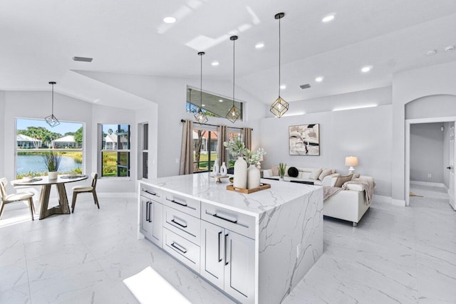 kitchen featuring hanging light fixtures, a kitchen island, light stone counters, lofted ceiling, and a water view