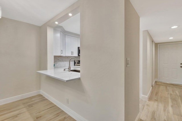 bar featuring decorative backsplash, light hardwood / wood-style floors, white cabinetry, and sink