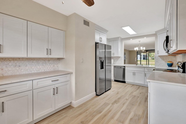 kitchen with decorative backsplash, appliances with stainless steel finishes, pendant lighting, light hardwood / wood-style flooring, and white cabinetry