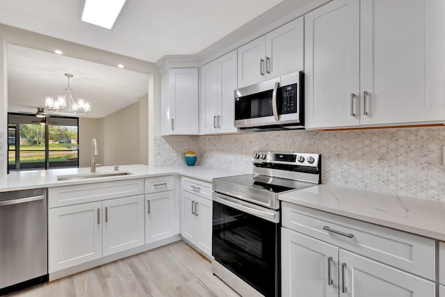 kitchen with white cabinets, sink, light hardwood / wood-style floors, stainless steel appliances, and a chandelier