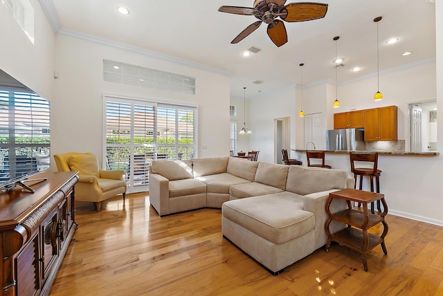 living room with crown molding, a towering ceiling, ceiling fan, and light wood-type flooring