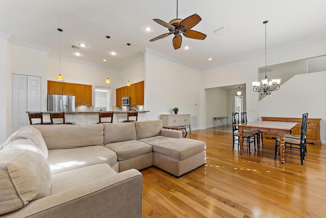 living room featuring ceiling fan with notable chandelier, a towering ceiling, ornamental molding, and light hardwood / wood-style floors