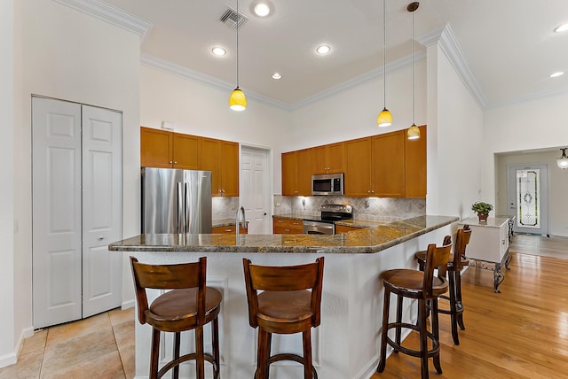 kitchen featuring stainless steel appliances, decorative light fixtures, kitchen peninsula, and dark stone counters