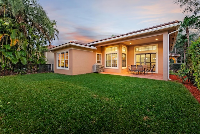 back house at dusk featuring a yard and a patio