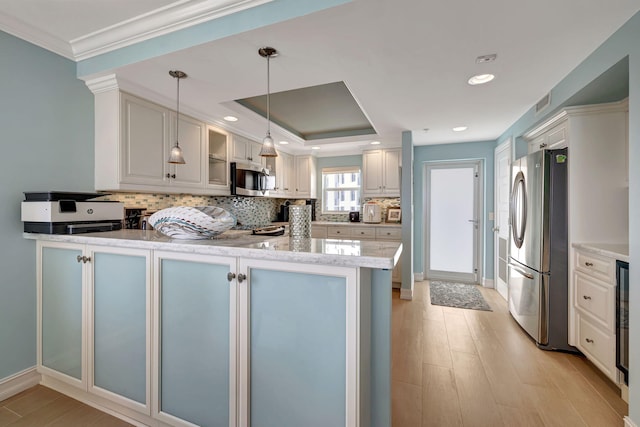 kitchen with appliances with stainless steel finishes, decorative light fixtures, tasteful backsplash, a raised ceiling, and kitchen peninsula