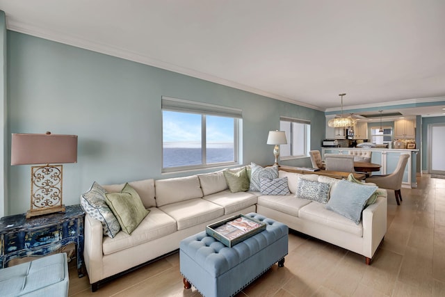 living room with light wood-type flooring, crown molding, a water view, and an inviting chandelier