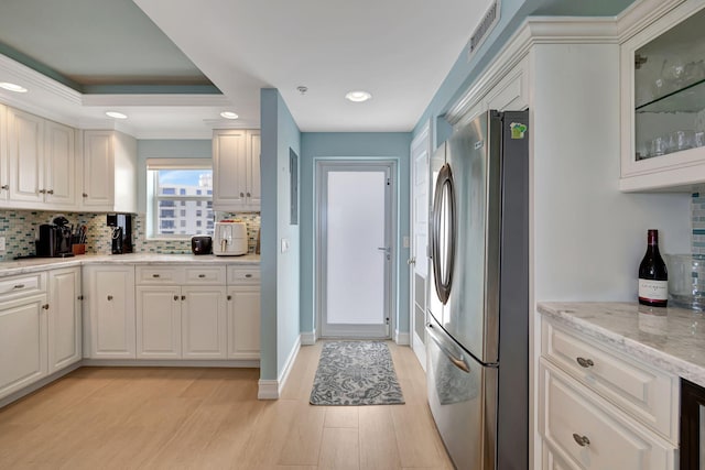 kitchen featuring a raised ceiling, backsplash, white cabinets, and stainless steel refrigerator